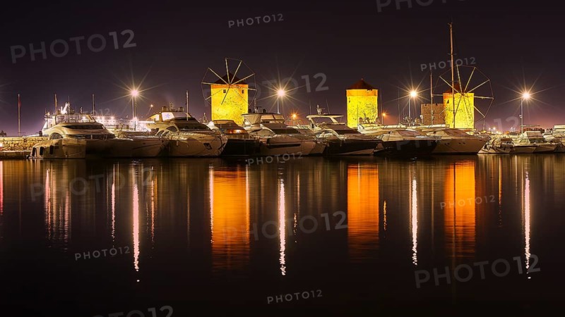 Oat at night with illuminated windmills and yachts reflected in the water, twilight, Mandraki harbour, Rhodes, Dodecanese, Greek Islands, Greece, Europe