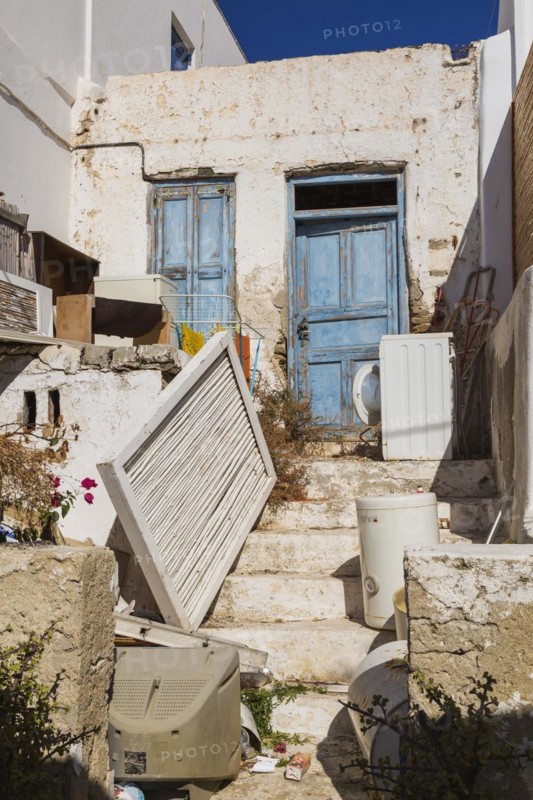 Discarded items in front yard of abandoned traditional house with blue wooden entrance door, Mykonos Town, Mykonos Island, Greece, Europe
