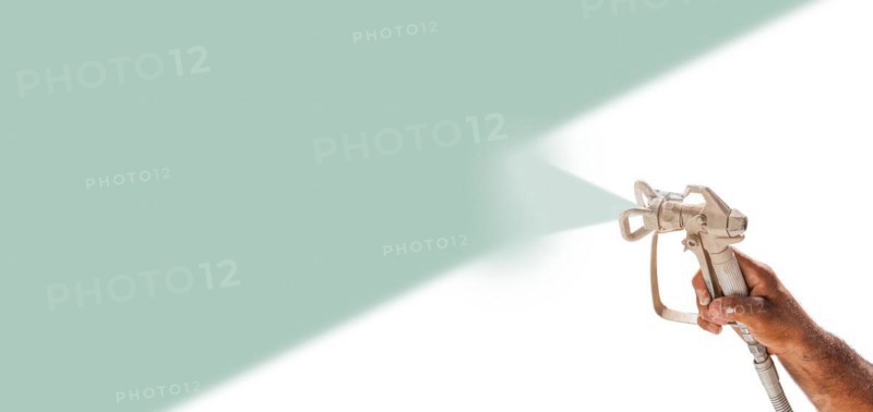 Professional spray painter holding spray gun spraying teal over white surface