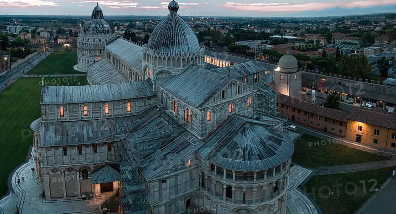 View of the illuminated Cathedral of Santa Maria Assunta with several domes at dusk with an atmospheric sky in Pisa, Pisa Italy Europe
