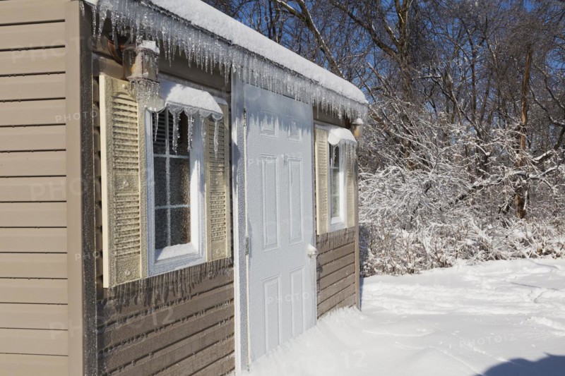 Storage shed facade covered in thick ice and snow in residential backyard after ice storm in early spring, Quebec, Canada, North America