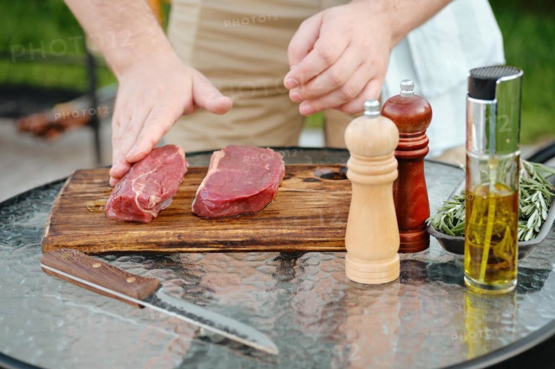Unrecognizable man rubbing olive oil with hand over raw beef strip steak