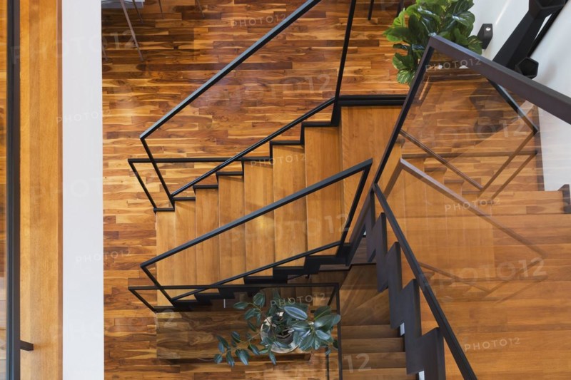 Top view of black powder coated steel L-shaped staircase with stained and varnished wooden steps and tempered glass handrail inside contemporary home with acacia wood flooring, Quebec, Canada, North America