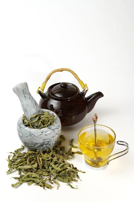 Lemon verbena infusion in a glass cup with a marble mortar and pestle and a ceramic teapot with dried lemon verbena leaves isolated on white background and copy space