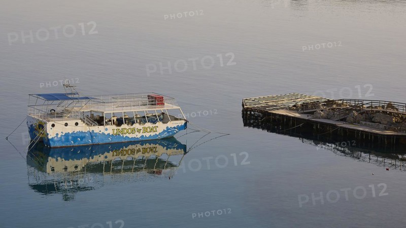 An excursion boat is reflected in the calm waters next to a wooden jetty, Lindos, Rhodes, Dodecanese, Greek Islands, Greece, Europe