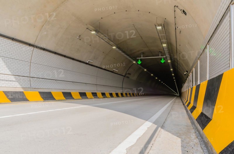 Two lane highway tunnel of white concrete with florescent lights and green arrows on ceiling and electrical cables running down the side wall in South Korea
