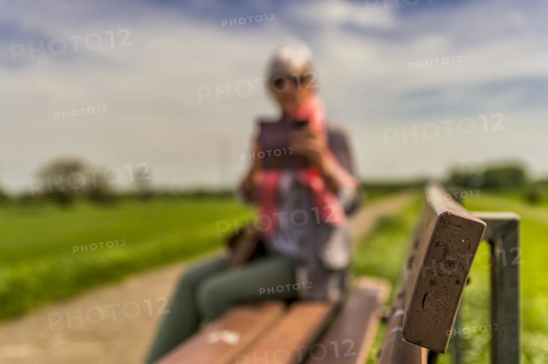 Senior citizen sitting on a bench and looking at her smartphone, side view, blurred, dike crest, Rhine, Zons, North Rhine-Westphalia, Germany, Europe