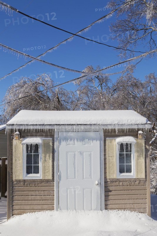 Storage shed facade and overhead electrical wires covered in thick ice and snow in residential backyard after ice storm in early spring, Quebec, Canada, North America