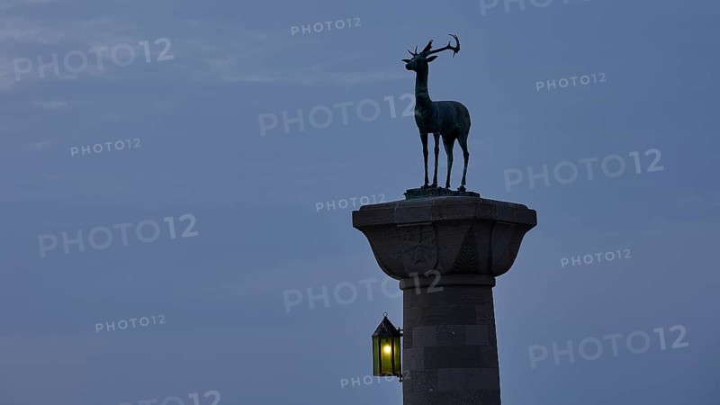 Deer statue on column with illuminated lantern at dusk, Mandraki Oat, Rhodes, Dodecanese, Greek Islands, Greece, Europe