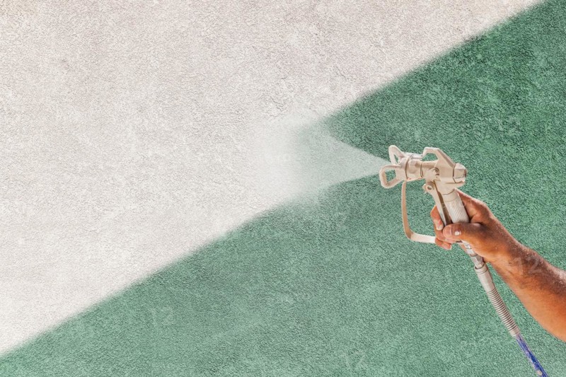 Professional spray painter holding spray gun spraying white paint over teal stucco surface