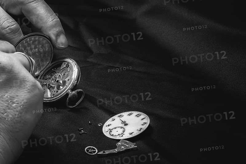 Opened pocket watch is repaired, dial and inner parts visible, on black fabric