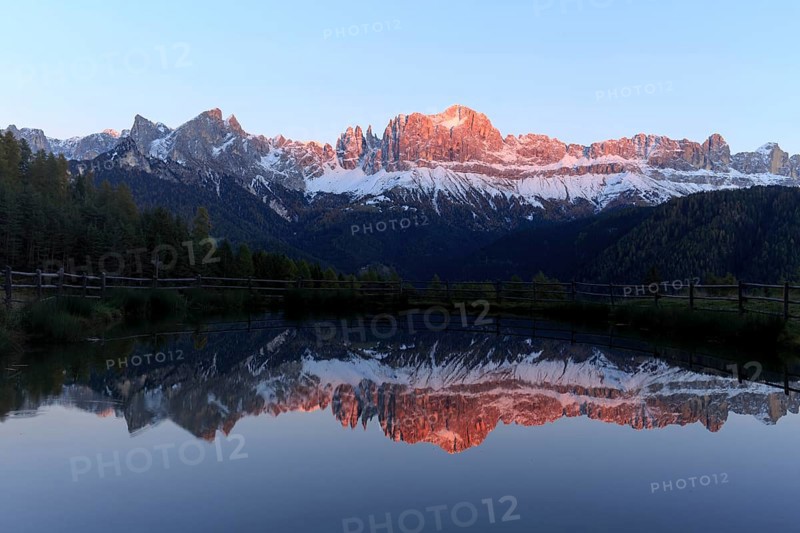 Early morning light illuminates a mountain range reflected in a still lake, Trentino-Alto Adige, Alto Adige, Bolzano province, Dolomites, Reflection rose garden at Wuhnleger Lake, San Cipriano