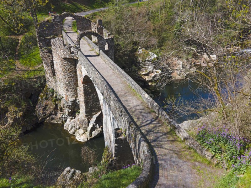 Old arched bridge over a river, bordering paths and nature in the sunlight, Bridge of the Devil, Pont de Diable, Romanesque stone bridge, Ariege river, Montoulieu, Ariege, France, Europe