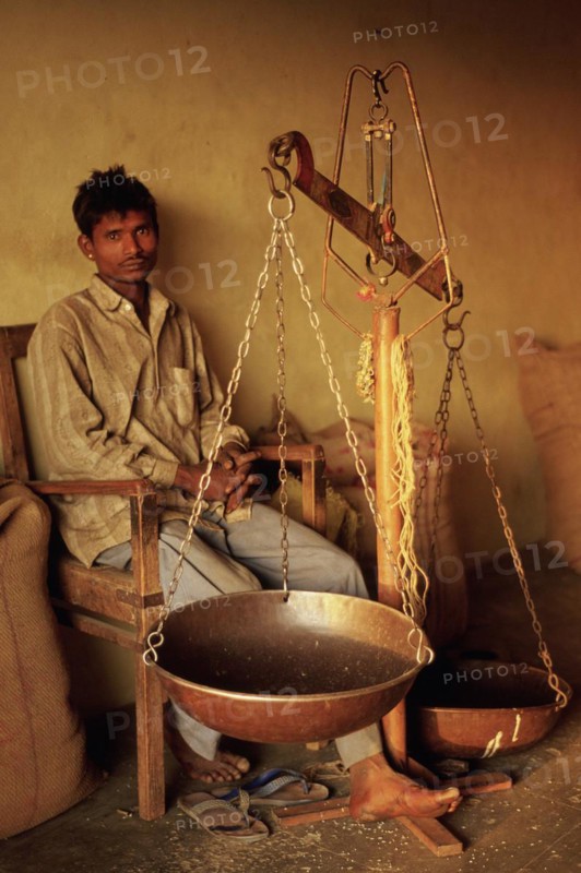Man, employee, working in a shop, rural India. His job is to weight the wheat that is sold to the clients. He belongs to a low caste