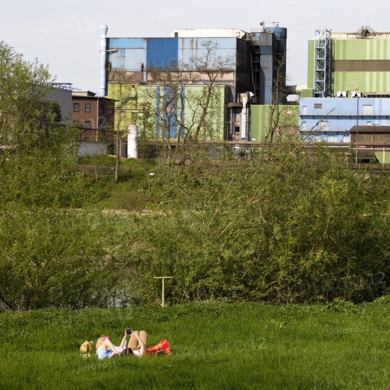 Couple lies on the Ruhrauen in front of the stainless steel plant in Witten, Ruhr area, North Rhine-Westphalia, Germany, Europe