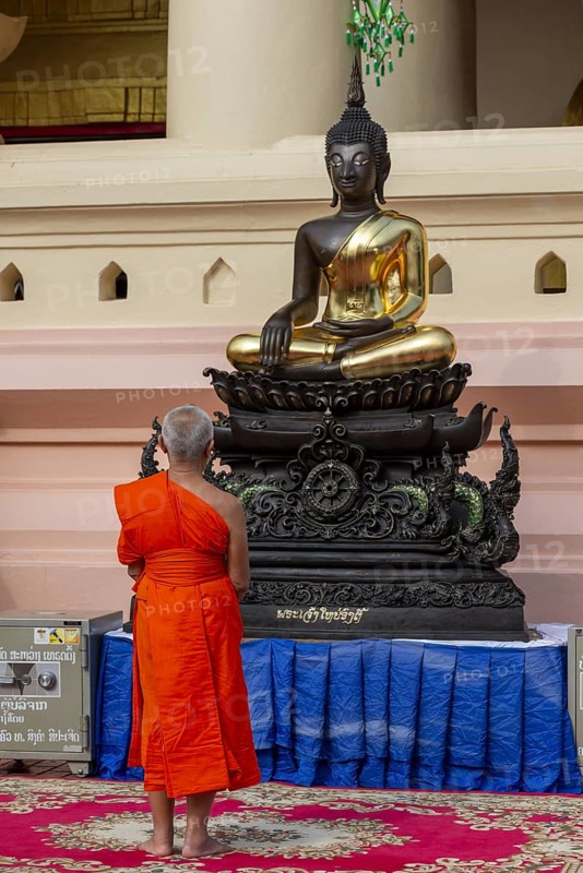 Monk in front of a Buddha statue, Bhumispara-mudra, Buddha Gautama at the moment of enlightenment, Wat Ong Teu, Vientiane, Laos, Asia