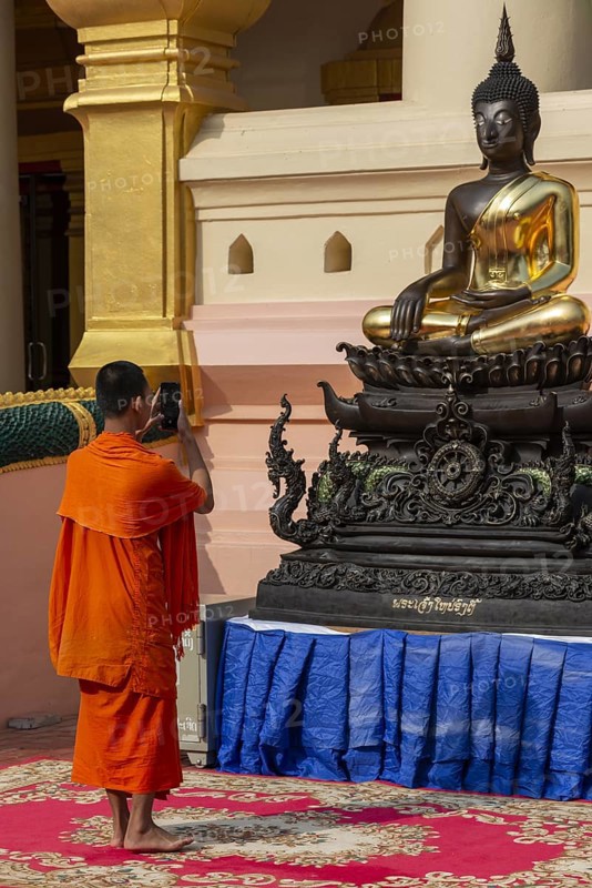 Monk in front of a Buddha statue, Bhumispara-mudra, Buddha Gautama at the moment of enlightenment, Wat Ong Teu, Vientiane, Laos, Asia