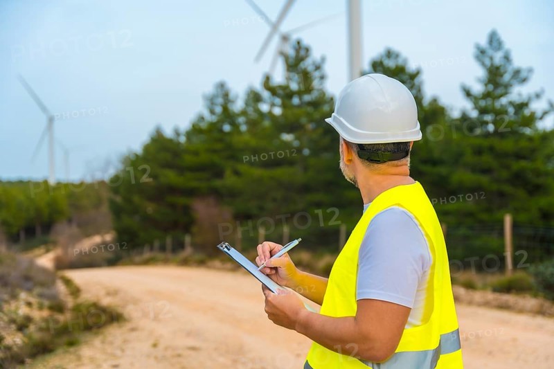 Rear view of a male mature engineer writing notes inspecting wind turbines in a green energy park