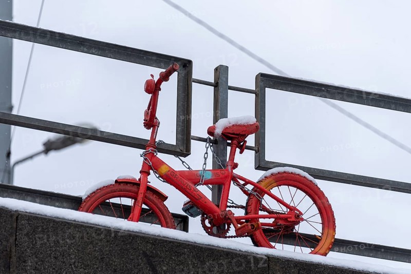 Red children's bicycle in the snow, attached to a bridge railing, Riga, Latvia, Europe