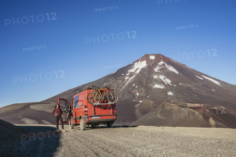 Young woman and her campervan in front of the Lonquimay volcano, Lonquimay volcano, Malalcahuello National Reserve, Curacautin, Araucania, Chile, South America