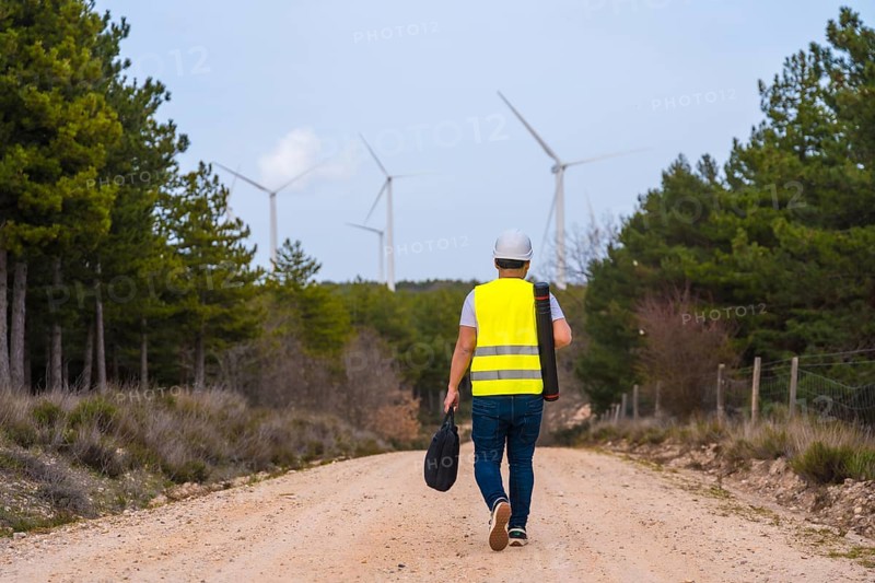 Rear view of a mature caucasian male worker walking along a path in a green energy park with wind turbines