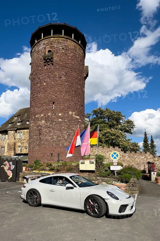 Porsche 911 GT3 stands in front of 13th century castle today Burghotel Trendelburg with castle tower, Trendelburg, Weserbergland, Hesse, Germany, Europe