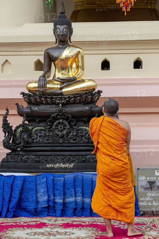 Monk in front of a Buddha statue, Bhumispara-mudra, Buddha Gautama at the moment of enlightenment, Wat Ong Teu, Vientiane, Laos, Asia