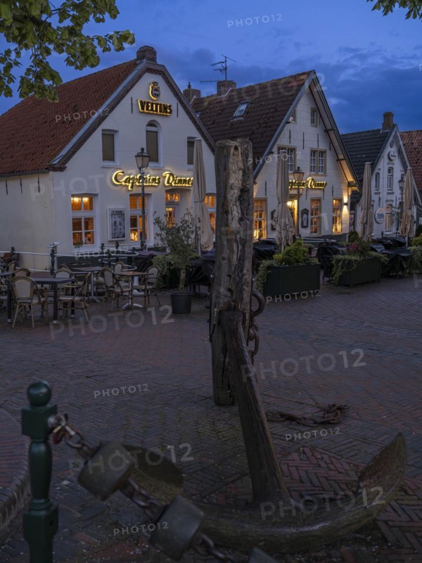 Ship's anchor on a wooden pile in front of restaurants at Greetsiel harbour at night, Greetsiel, Krummhoern, East Frisia, Lower Saxony, Germany, Europe