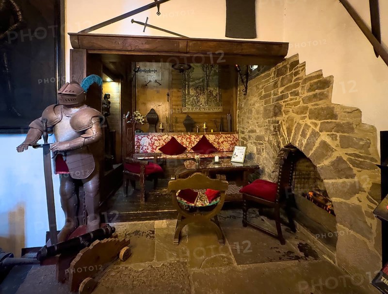 Fireplace corner sitting area with fireplace in entrance area of 13th century castle today Burghotel Trendelburg with fireplace embedded in wall on the right, historical knight's armour on the left, Trendelburg, Weserbergland, Hesse, Germany, Europe