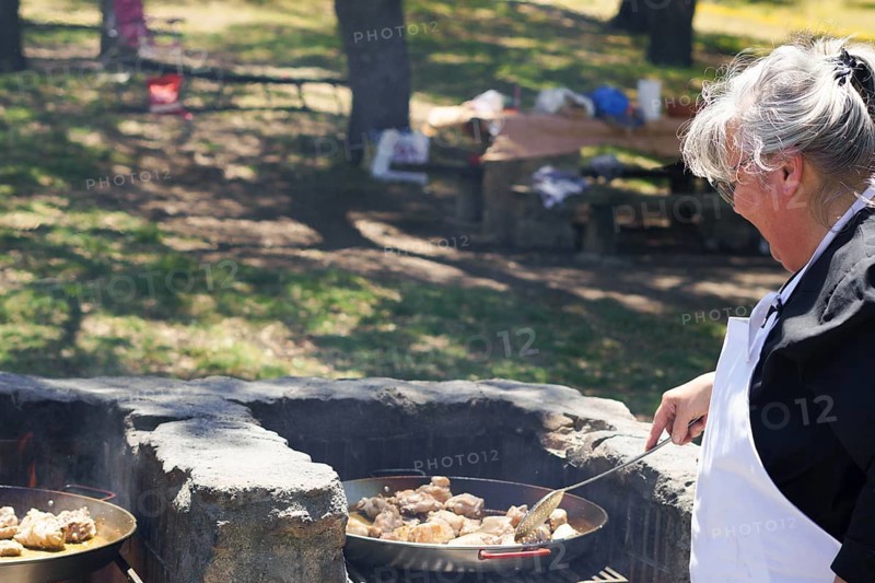Woman cook in a white apron preparing a paella on the fire in the field