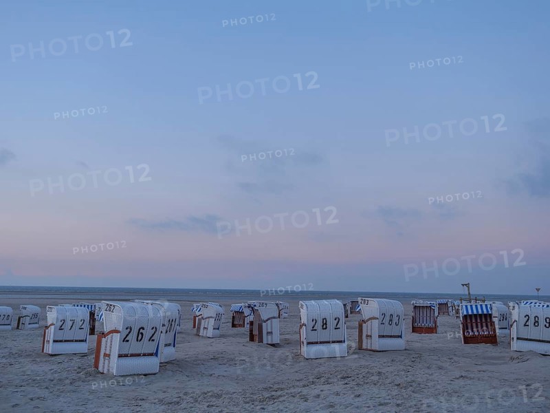 A quiet beach with white beach chairs and a gentle sunset in the sky, setting sun on a beach with beach chairs and clouds in the sky, spiekeroog, germany