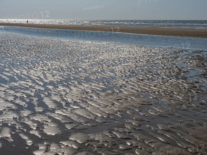Close-up of a sandy beach with watercourse and waves in the background, glittering sea water at low tide on the beach, de haan, belgium