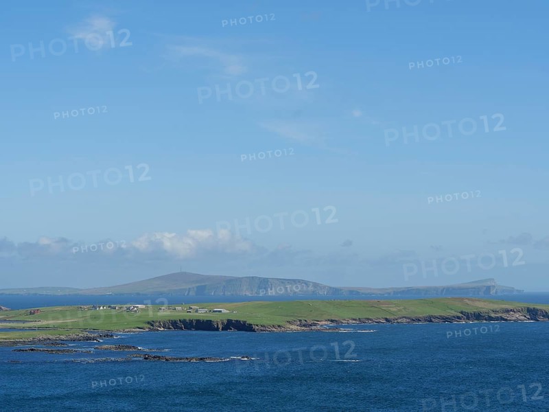 Vast coastal landscape with blue sky and green hills on the horizon, green meadows on a deep blue sea and a rocky coastline with individual houses, lerwick, shetland, Scotland, United Kingdom, Europe