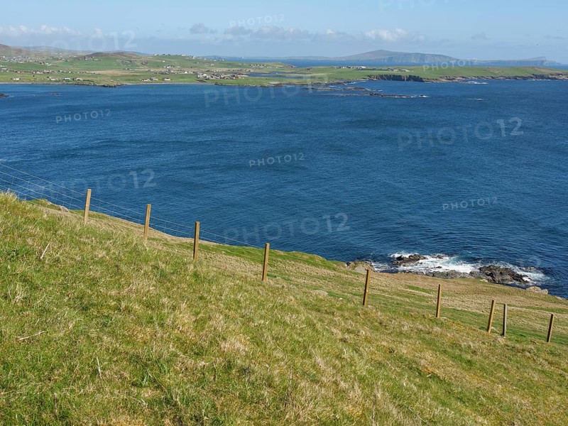 Green meadow leads to rocky coastline with sweeping views across deep blue sea, green meadows by a deep blue sea and a rocky coastline with individual houses, lerwick, shetland, Scotland, United Kingdom, Europe
