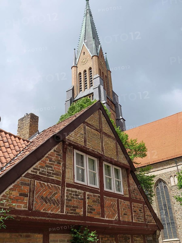 A half-timbered house in front of a high church tower, cloudy sky and a red tiled roof, large church towers with trees and historic houses in the foreground, Schleswig, Germany, Europe