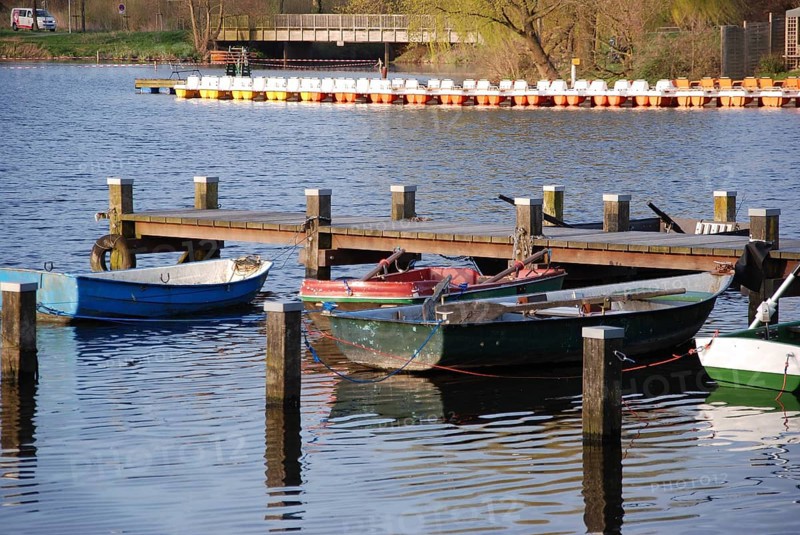 Small boats are moored on wooden jetties, calm water, in spring and under a blue sky, rowing boats and pedal boats on a small wooden jetty in the lake surrounded by trees, Borken Germany