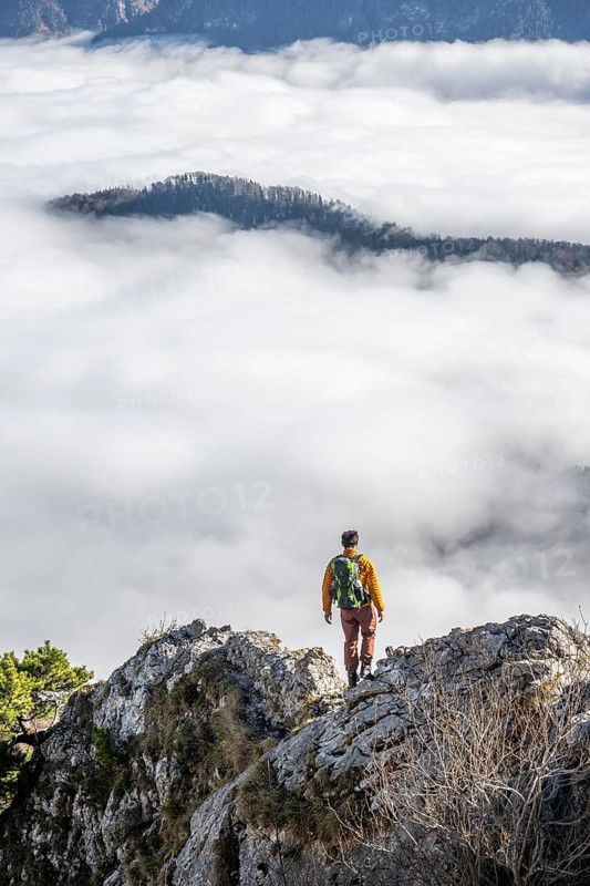 Hiker at Ettaler Manndl, view over mountain landscape and sea of clouds, high fog in the valley, Ammergau Alps, Bavaria, Germany, Europe