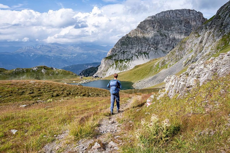 Mountaineer in front of mountain landscape, mountain hut Obstanserseehuette at the mountain lake Obstansersee, behind rocky mountain peak Rosskopf, Carnic main ridge, Carnic High Trail, Carnic Alps, Carinthia, Austria, Europe