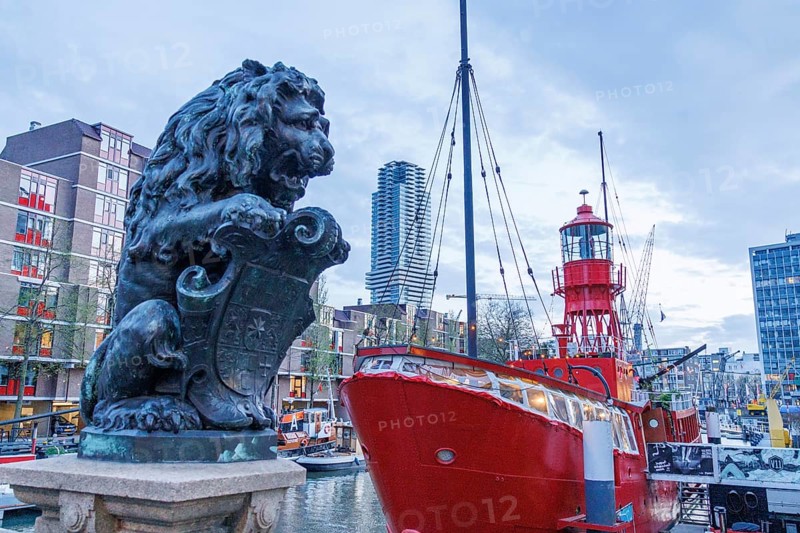 A lion statue in a harbour next to a red ship and modern buildings under a clear sky, small harbour in a big city with a lighthouse and modern houses, Rotterdam, Netherlands