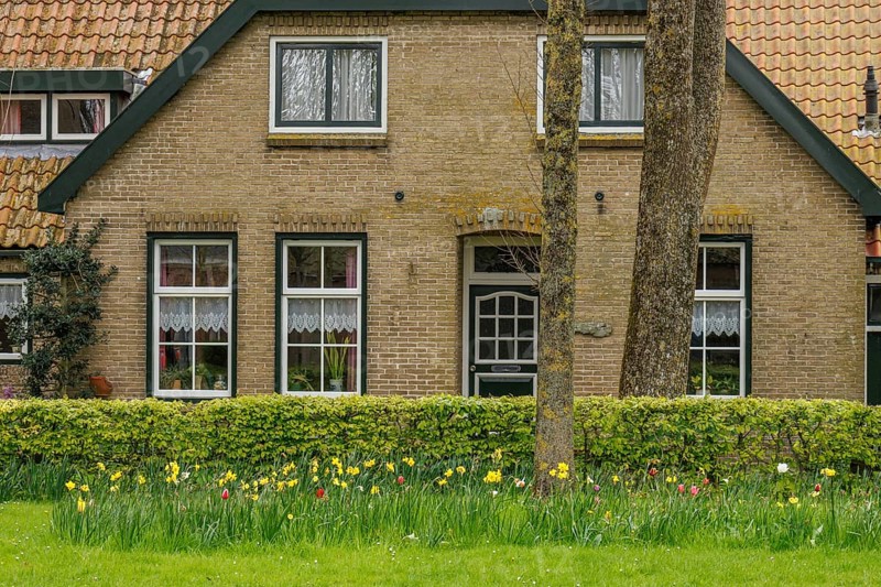 Front view of a cosy brick house with flower bed and green lawn, old houses with green gardens in a small village, nes, ameland, the netherlands