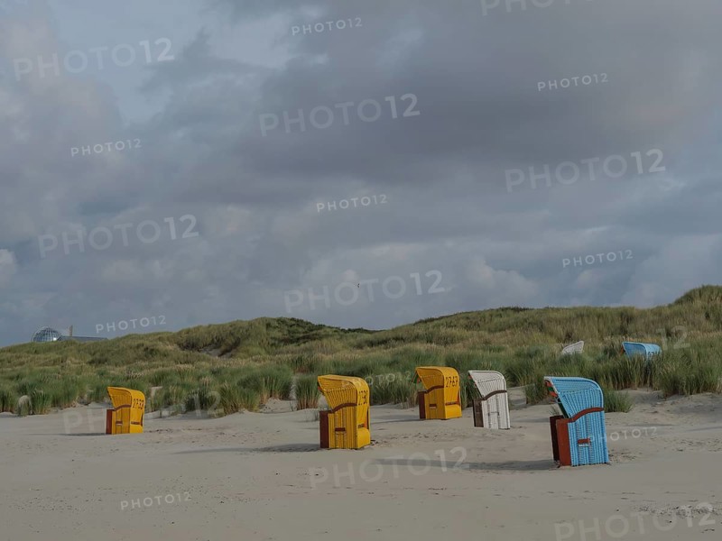 Beach chairs scattered on the beach under a cloudy sky, surrounded by gentle dunes, colourful beach chairs on the beach and in the dunes under an overcast sky, red wooden boat and yellow beach chair, Juist, Germany, Europe