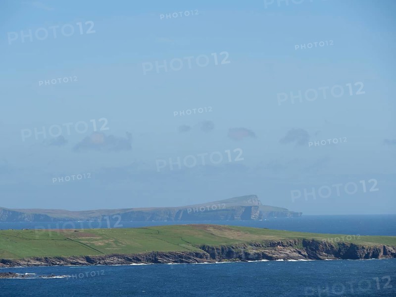 Wide green fields meet the deep blue sea, with a visible island in the background, green meadows on a deep blue sea and a rocky coastline with individual houses, lerwick, shetland, Scotland, United Kingdom, Europe
