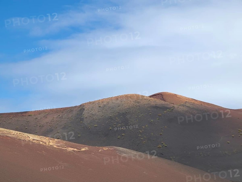 Dry, hilly desert area under a blue sky with white clouds, barren landscape of lava mountains, lanzarote, spain