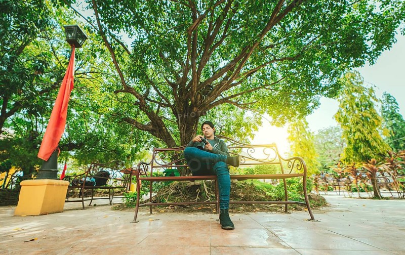 Photographer sitting on a bench checking his camera. Male photographer checking dslr camera sitting on a bench