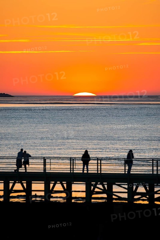 Silhouettes of several people on the pier free canal, jetty, couple and individuals watching the picturesque, golden, breathtakingly beautiful sunset over the sea, last moments in front of the sun sets in the sea, island Langluetjen II on the left edge of the picture on the horizon, orange glowing cloudless sky, wide sea in soft colours, mouth of the Weser into the North Sea, Outer Weser, Bremerhaven, Land Bremen, Germany, Europe