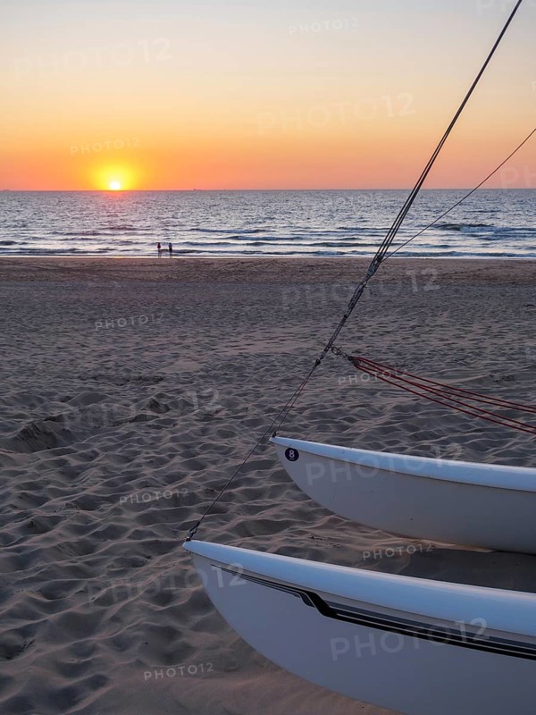 Boats on the beach at sunset, the sea glistens under the orange sky, a calm and relaxed atmosphere, sunset on the sea with boats and a bench, sand on the beach, de Haan, Belgium, Europe
