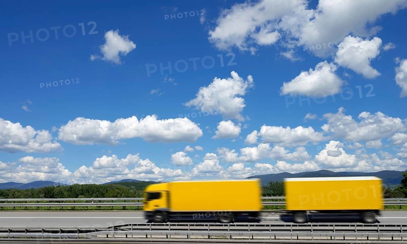 A yellow lorry drives on the A3 motorway under a blue sky with white clouds, motion blur, Bavarian Forest in the background, Deggendorf, Bavaria, Germany, Europe