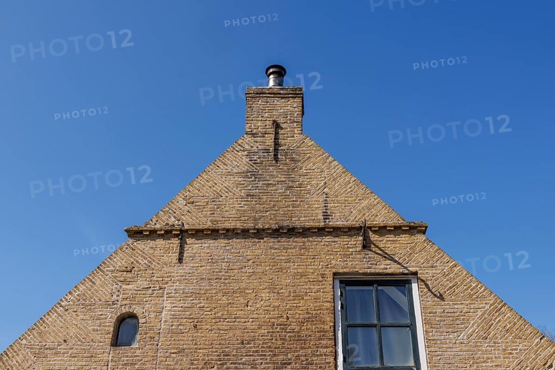 Brick house facade with chimney in front of a clear blue sky, minimalist look, historic houses in a small village with small streets and trees in spring, Nes, Ameland, Netherlands