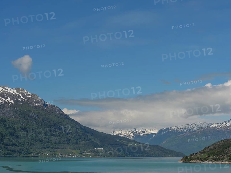 Calm waters with snow-capped mountains under a clear blue sky, greenish shimmering water in a fjord with snow-capped mountains and green trees, eidfjord, Norway, Europe