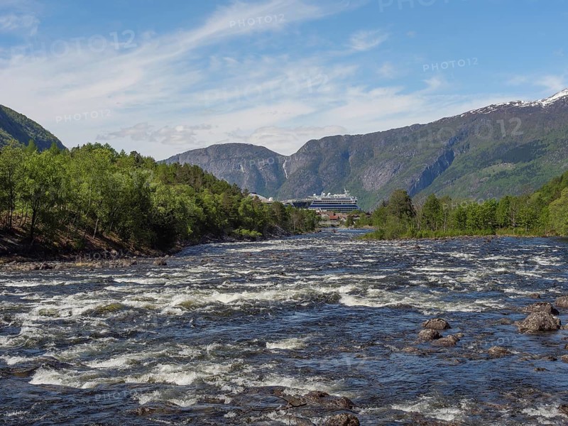 A river in a valley, surrounded by green forests and mountains, in the background a large ship, wild river in a fjord with snow-capped mountains and green trees, eidfjord, Norway, Europe